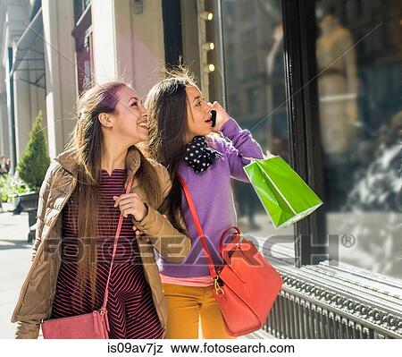 Stock Photo - Young female adult twins carrying shopping bags and looking at shop window. Fotosearch