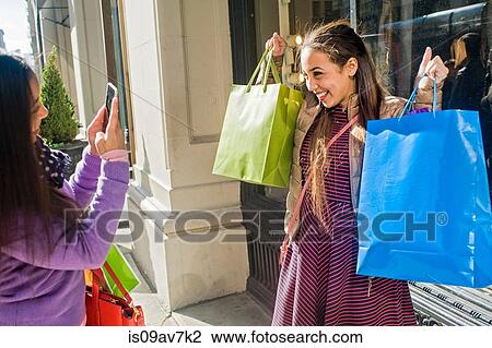 Young female adult twins in city photographing each other with shopping bags on smartphone View Large Photo Image Stock Image - Young female adult twins in city photographing each other with shopping bags on smartphone. Fotosearch