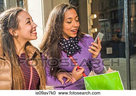 Young female adult twins in city with shopping bags reading smartphone text View Large Photo Image Stock Image - Young female adult twins in city with shopping bags reading smartphone text. Fotosearch