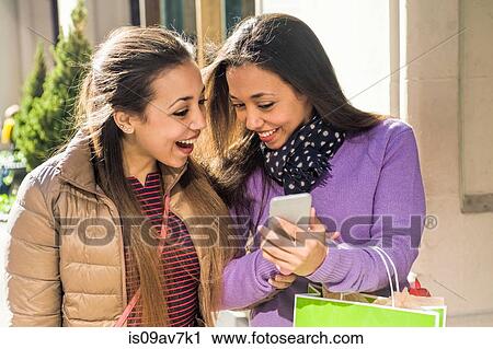 Young female adult twins in city with shopping bags laughing at smartphone text View Large Photo Image Stock Image - Young female adult twins in city with shopping bags laughing at smartphone text. Fotosearch