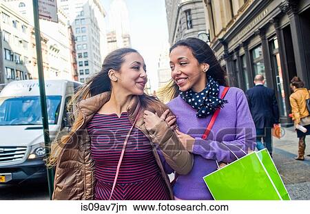 Young female adult twins with shopping bags strolling and chatting on city street View Large Photo Image Picture - Young female adult twins with shopping bags strolling and chatting on city street. Fotosearch