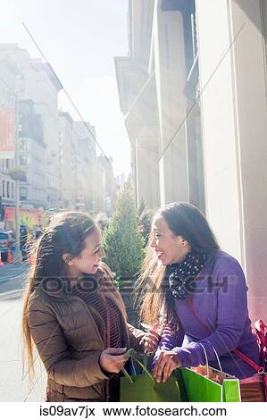 Stock Photo - Young female adult twins with shopping bags chatting and laughing on city sidewalk. Fotosearch