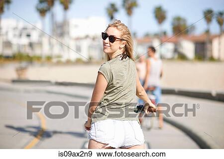 Young female cyclist looking over her shoulder whilst cycling at Venice Beach, Los Angeles, California, USA View Large Photo Image Stock Photo - Young female cyclist looking over her shoulder whilst cycling at Venice Beach, Los Angeles, California, USA. Fotosearch