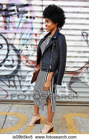 Stock Photography - Young female fashion blogger with afro hair by graffiti wall, New York, USA. Fotosearch