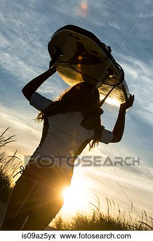 Young girl at beach, carrying surfboard, at sunset, rear view View Large Photo Image Stock Photo - Young girl at beach, carrying surfboard, at sunset, rear view. Fotosearch