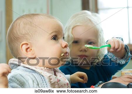 Young girl feeding baby sister with spoon View Large Photo Image Stock Photo - Young girl feeding baby sister with spoon. Fotosearch