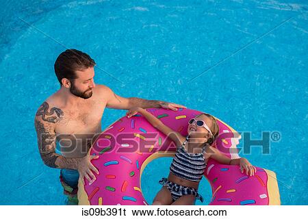 Young girl in swimming pool, relaxing on inflatable ring, father standing beside her View Large Photo Image Stock Photograph - Young girl in swimming pool, relaxing on inflatable ring, father standing beside her. Fotosearch