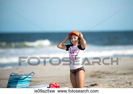 Stock Photo - Young girl on beach putting cap on. Fotosearch