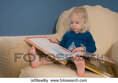 Young girl sitting in armchair, looking at book View Large Photo Image Stock Photo - Young girl sitting in armchair, looking at book. Fotosearch