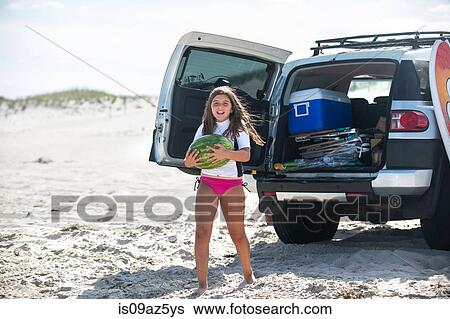 Young girl standing at back of open vehicle, holding melon View Large Photo Image Stock Photograph - Young girl standing at back of open vehicle, holding melon. Fotosearch