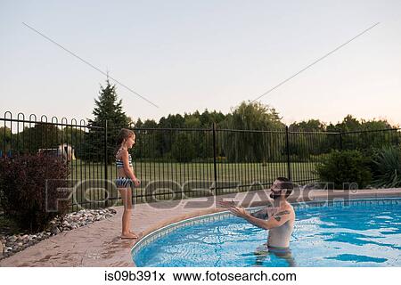 Young girl standing on edge of swimming pool, father in pool encouraging her to jump in View Large Photo Image Stock Photo - Young girl standing on edge of swimming pool, father in pool encouraging her to jump in. Fotosearch