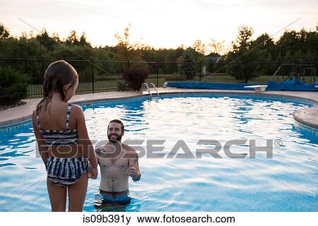 Stock Photo - Young girl standing on edge of swimming pool, father in pool encouraging her to jump in. Fotosearch