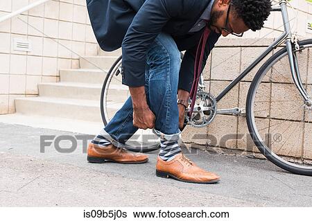Stock Photograph - Young male cyclist rolling down jeans on railway station platform. Fotosearch