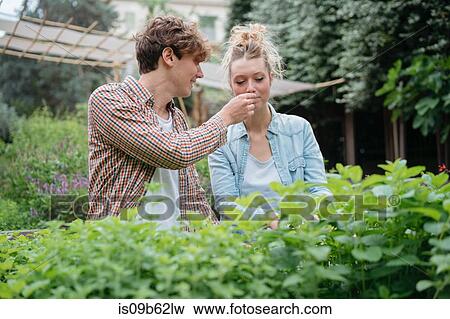 Stock Photo - Young man and woman in garden, young man holding plant for woman to smell. Fotosearch