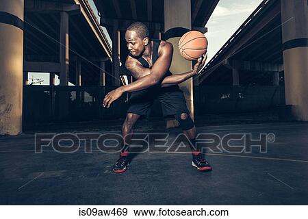 Stock Photo - Young man bending forward balancing basketball on hand, looking away. Fotosearch