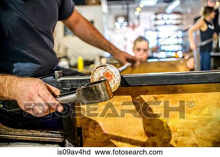 Stock Image - Young man blowing glass, mid section, close-up. Fotosearch