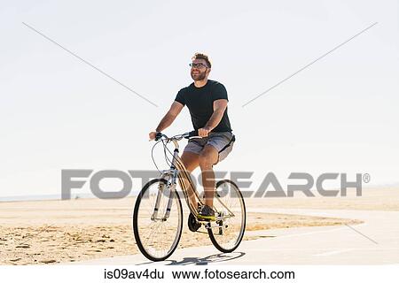 Young man cycling along pathway at beach View Large Photo Image Stock Photograph - Young man cycling along pathway at beach. Fotosearch