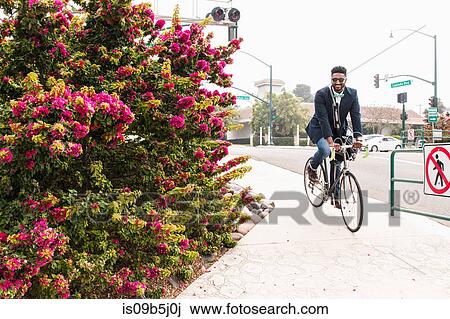 Stock Image - Young man cycling onto rail station platform. Fotosearch