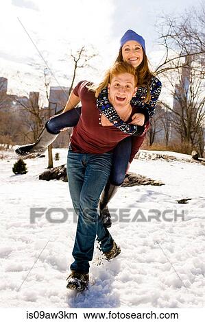 Picture - Young man giving girlfriend a piggy back in snowy Central Park, New York, USA. Fotosearch