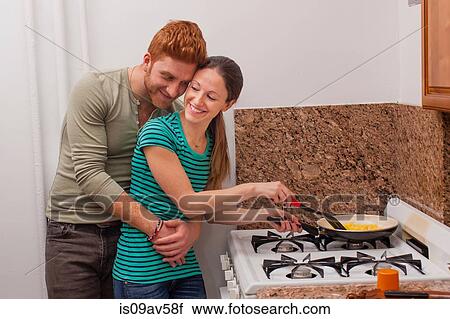 Young man in kitchen arms around young woman cooking on hob smiling View Large Photo Image Stock Image - Young man in kitchen arms around young woman cooking on hob smiling. Fotosearch
