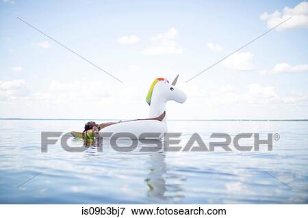 Stock Photo - Young man lying back on inflatable unicorn in sea, Santa Rosa Beach, Florida, USA. Fotosearch