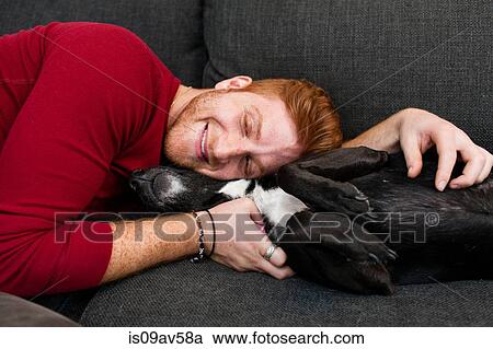 Young man lying on sofa hugging pet dog eyes closed smiling View Large Photo Image Stock Image - Young man lying on sofa hugging pet dog eyes closed smiling. Fotosearch