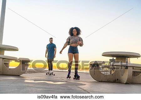 Young man on skateboard, following mid adult woman on rollerskates View Large Photo Image Stock Image - Young man on skateboard, following mid adult woman on rollerskates. Fotosearch