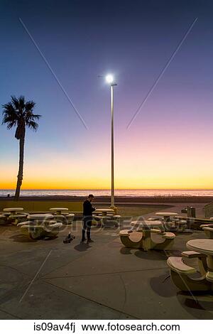 Young man, outdoors at sunset, using smartphone View Large Photo Image Stock Image - Young man, outdoors at sunset, using smartphone. Fotosearch