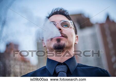 Stock Image - Young man outdoors, exhaling smoke. Fotosearch