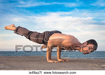 Stock Image - Young man outdoors, in yoga position, balancing on hands. Fotosearch