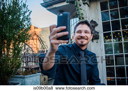 Stock Photo - Young man sitting outdoors, holding smartphone, on video call. Fotosearch