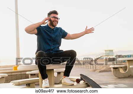 Stock Photo - Young man sitting outdoors, using smartphone, laughing. Fotosearch