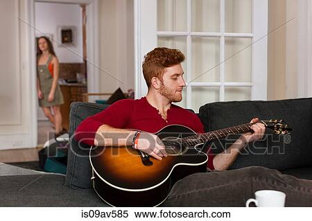 Young man sitting sofa playing guitar View Large Photo Image Stock Photography - Young man sitting sofa playing guitar. Fotosearch