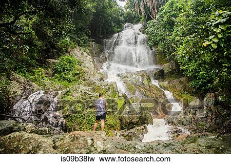 Young man standing on rock looking at Na Muang Waterfall, Koh Samui, Thailand View Large Photo Image Stock Photo - Young man standing on rock looking at Na Muang Waterfall, Koh Samui, Thailand. Fotosearch