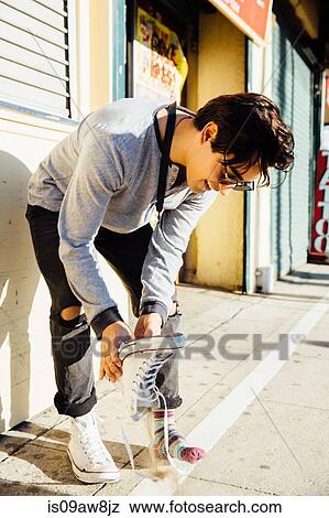 Stock Photo - Young man standing outdoors, emptying sand from shoe. Fotosearch