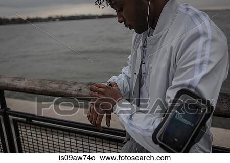 Picture - Young man training on riverside at dawn timing on smartwatch. Fotosearch