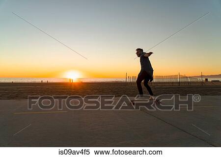 Young man using skateboard on pathway, beside beach, sunset View Large Photo Image Stock Photography - Young man using skateboard on pathway, beside beach, sunset. Fotosearch