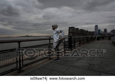 Stock Image - Young man warming up whilst training on riverside at dawn. Fotosearch