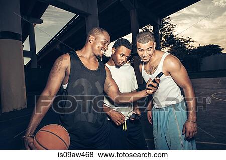 Young men holding basketball looking at smartphone smiling View Large Photo Image Stock Photo - Young men holding basketball looking at smartphone smiling. Fotosearch