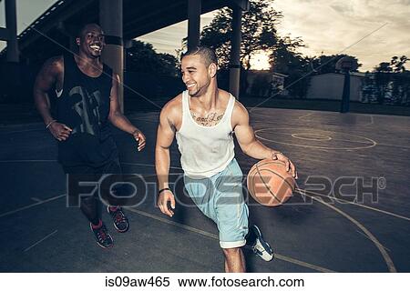 Stock Photography - Young men playing basket ball on basketball court smiling. Fotosearch