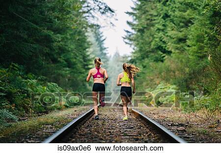 Stock Photograph - Young woman and teenage girl running on rural train track, rear view. Fotosearch