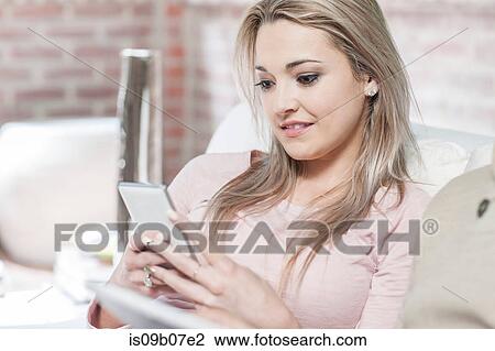Young woman at home, relaxing on sofa, looking at smartphone View Large Photo Image Stock Image - Young woman at home, relaxing on sofa, looking at smartphone. Fotosearch