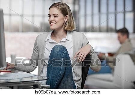 Stock Image - Young woman at home, working at desk, smiling. Fotosearch