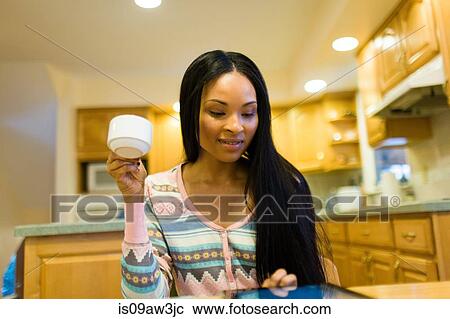 Young woman drinking coffee and reading digital tablet at kitchen table View Large Photo Image Stock Image - Young woman drinking coffee and reading digital tablet at kitchen table. Fotosearch