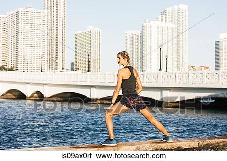 Stock Image - Young woman exercising by water's edge. Fotosearch