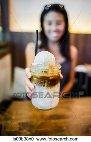 Stock Image - Young woman holding coffee float at Farm to Table, Bangkok, Thailand. Fotosearch