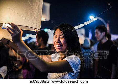 Young woman holding lit paper lantern waiting to release at Loy Krathong Paper Lantern Festival in Chiang Mai, Thailand View Large Photo Image Stock Photo - Young woman holding lit paper lantern waiting to release at Loy Krathong Paper Lantern Festival in Chiang Mai, Thailand. Fotosearch