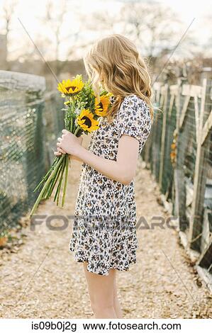 Stock Image - Young woman holding sunflowers, side view. Fotosearch