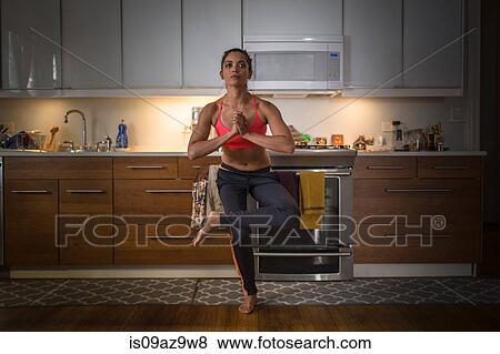 Stock Photo - Young woman in kitchen, in yoga position. Fotosearch
