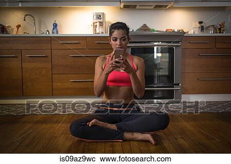 Young woman in kitchen, sitting in yoga position, using smartphone View Large Photo Image Stock Image - Young woman in kitchen, sitting in yoga position, using smartphone. Fotosearch